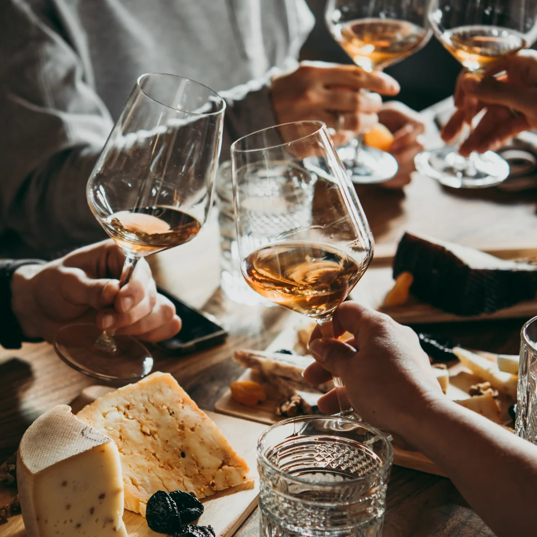 Persone che brindano con calici di vino durante una degustazione con tagliere di formaggi