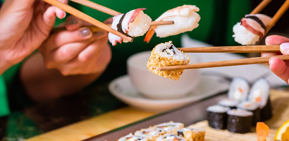 Mani con bacchette che sollevano pezzi di nigiri sushi da un vassoio