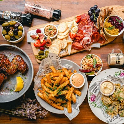 Tavolo visto dall'alto con alette di pollo, patatine, tagliere di salumi e altri antipasti da bistrot