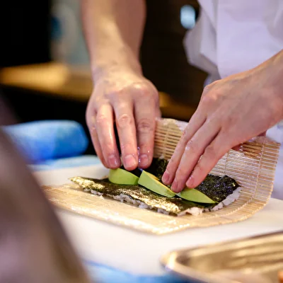 Mani di uno chef che preparano un rotolo di sushi su uno stuoino di bambù