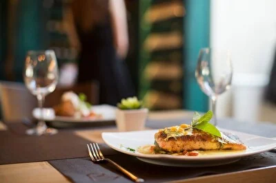 Filetto di salmone grigliato impiattato con erbe aromatiche, servito su un tavolo con calici di vino