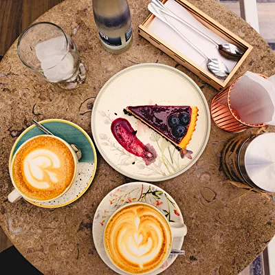 Vista dall'alto di due cappuccini con latte art, una fetta di torta e posate su un tavolo del bar