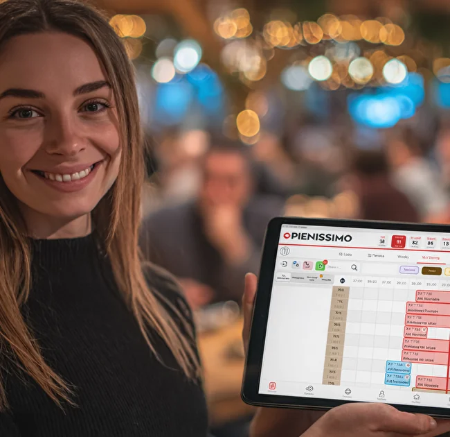 Cameriera che mostra su un tablet la dashboard con turni e prenotazioni del locale, in un ristorante affollato