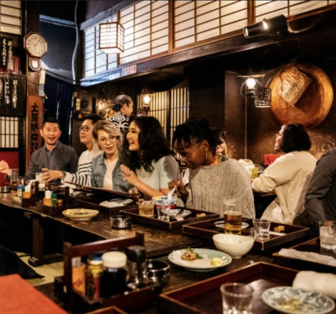 Clienti seduti al bancone di un ristorante giapponese tradizionale con lanterne e paraventi shoji